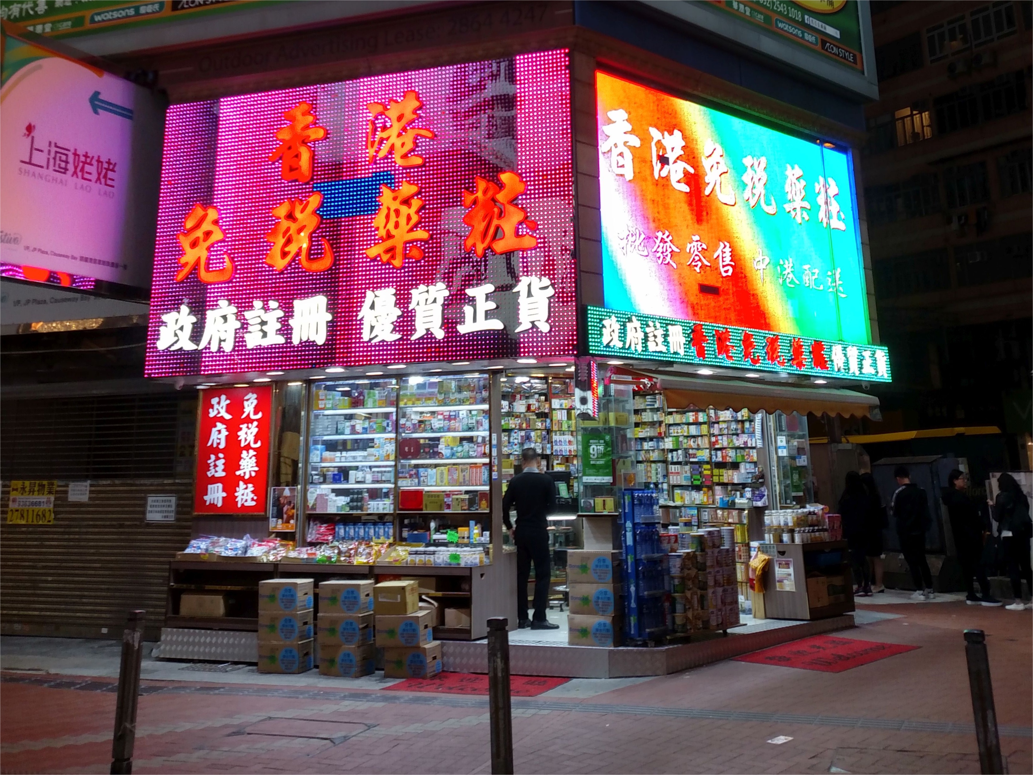 Neon signs illuminating a traditional Hong Kong street at night, with bustling storefronts and warm yellow lighting creating the typical atmospheric scene of the city